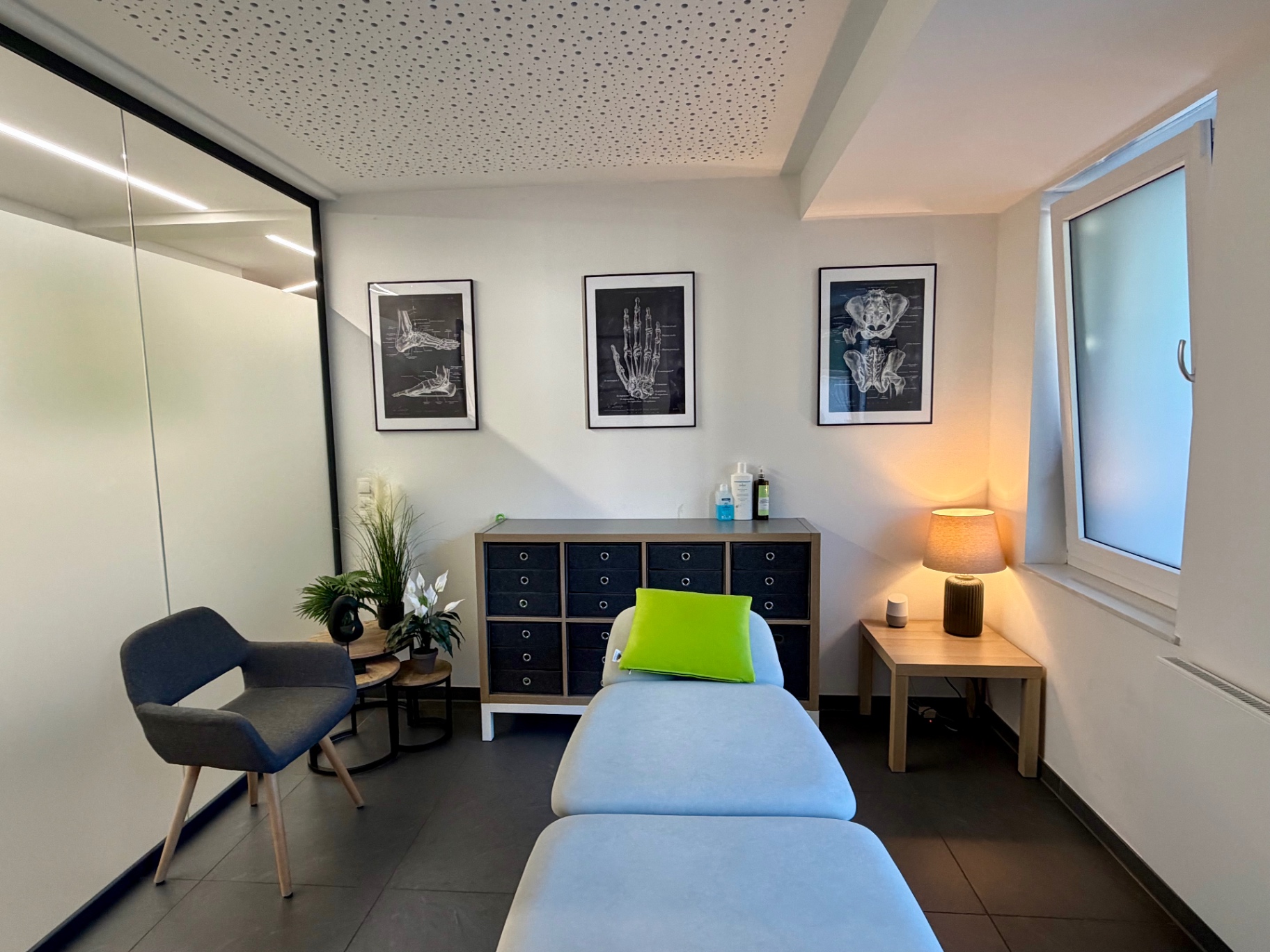 Behandlungsraum mit anatomischen Postern, hellblauer Liege und warmem Licht