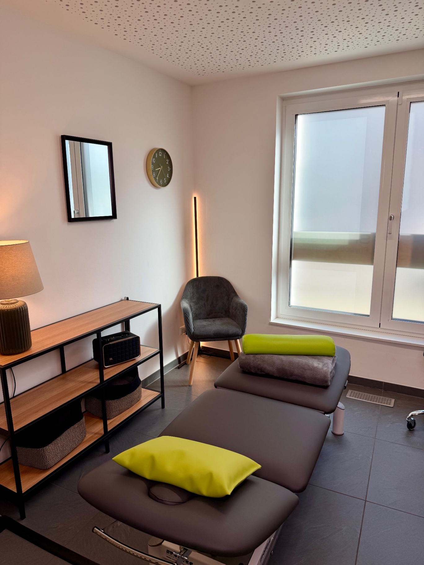 Ruhiger Behandlungsraum mit grauer Liege, Stehlampe und Sessel