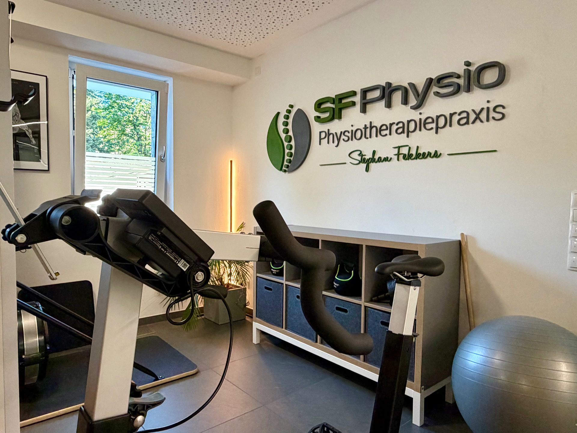 Trainingsbereich mit Ergometer, modernem Lichtkonzept und SF-Physio-Logo an der Wand